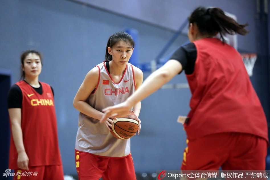 训练馆内气氛火热，女篮姑娘们在进行拉伸训练，神情专注而坚定，肌肉线条在灯光下显得格外有力，仿佛每一根纤维都在为即将到来的硬仗做着准备。