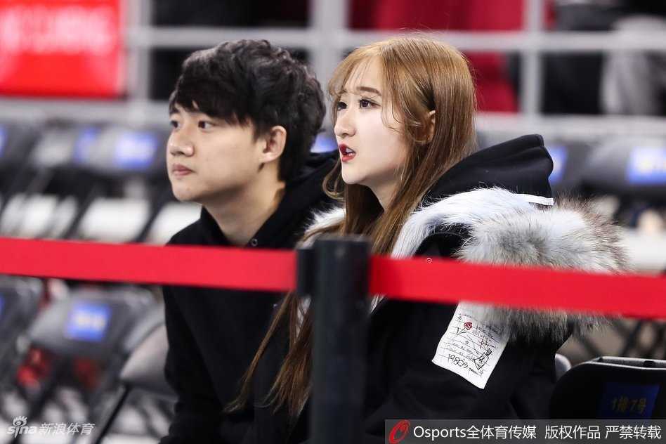 戴着眼镜的知性女球迷，在人声鼎沸的环廊中回眸一笑，手中紧握的助威棒透露出她对这支球队毫无保留的支持，文静与狂热在此刻完美交融。