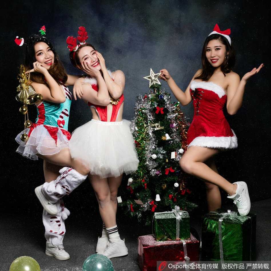 京城圣诞夜的冰雪热舞 篮球宝贝定格冬日活力瞬间 一位篮球宝贝安静地站在巨大的金色圣诞树前,双手交叠,笑容温婉,背景的灯光映衬出她柔美的轮廓,画面静谧而温馨。