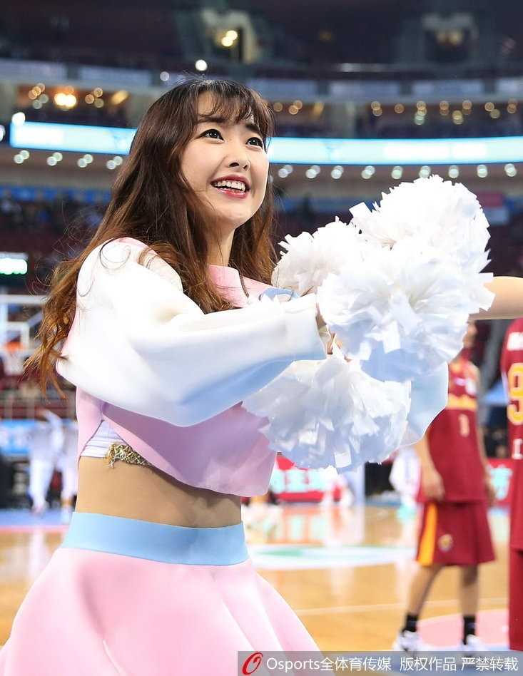 京城篮坛的靓丽风景:首钢主场大胜之夜,篮球宝贝热舞助威 特写镜头捕捉到一位篮球宝贝的甜美笑容,她手持彩色花球,眼眸中闪烁着舞台灯光的光芒,青春的气息与赛场的热血在此刻完美交融。