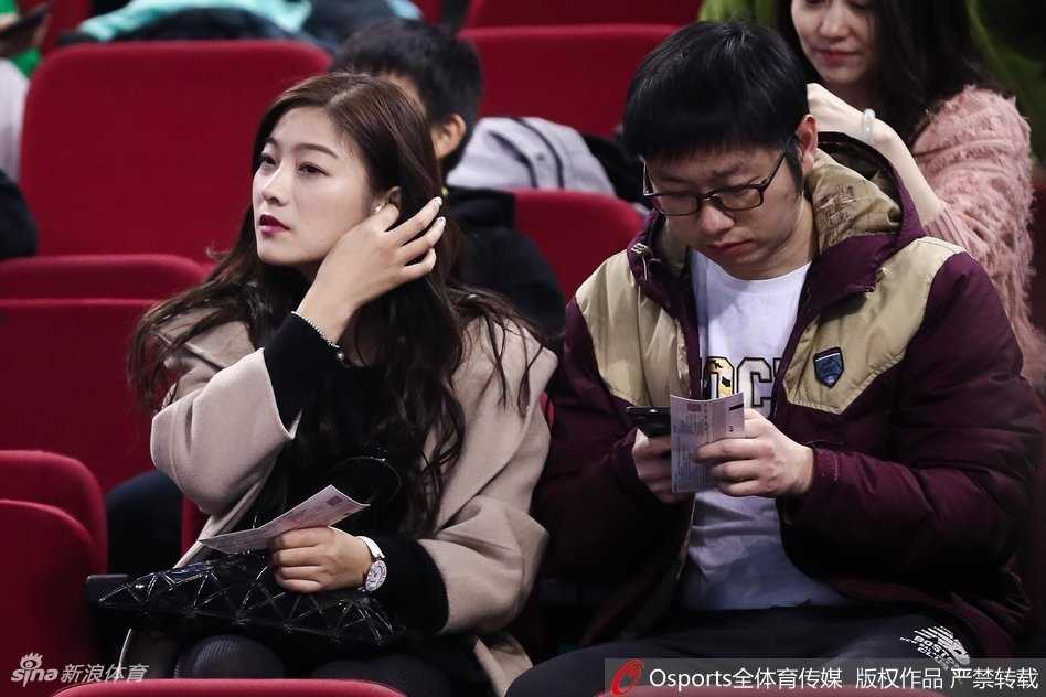 京城篮球之夜,美女球迷点亮看台风景线 一位长发美女站在看台通道处回眸,眼神中带着一丝笑意。她身穿简约的深色外套,身后是涌动的人群和赛场明亮的灯光,整个画面充满了动态的美感,仿佛定格了比赛间隙的一个迷人瞬间。