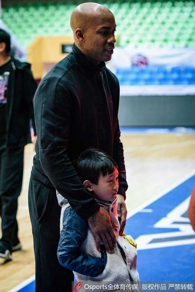 京城篮球最后的温情:马布里披北控战袍与小球迷互动,开启赛季新征程 马布里双手抱胸与一位扎着马尾辫的小女孩站在一起,小女孩略显羞涩地比划着爱心手势,老马则低头注视着她,画面定格在刚硬与童真的温柔碰撞瞬间。
