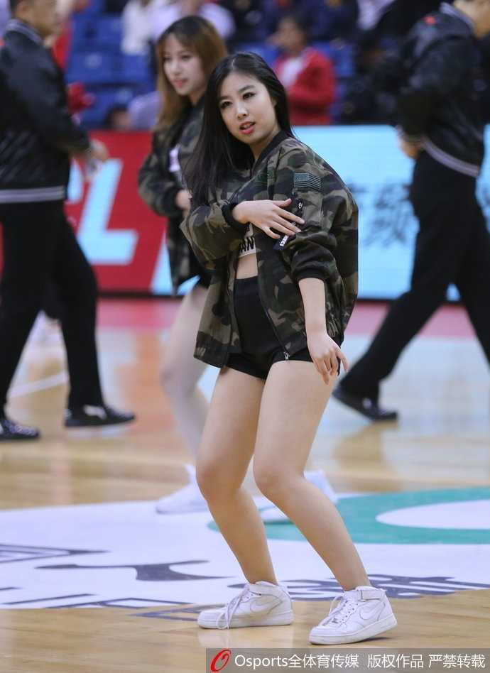 光影之外的舞者:青岛啦啦队与她们的CBA赛场故事 一位青岛啦啦队员在表演间隙独自站在场边,她扎着高马尾,若有所思地看向远方,身后的看台上坐满了热情的观众。这张照片展现了篮球宝贝在喧闹赛场中难得一见的安静与柔美。
