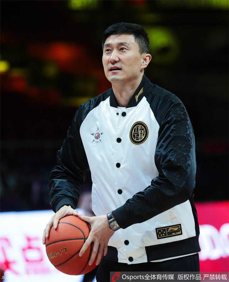 杜锋在场边接受媒体采访，手里拿着战术板，但目光不时看向一旁玩耍的儿子，神情专注而又夹杂着一丝作为父亲的牵挂。