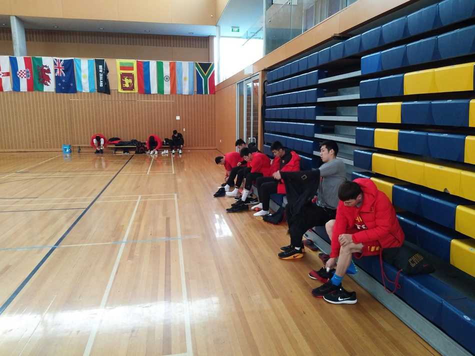 南半球的寒冬热练 中国男篮蓝队新西兰拉练穿上棉衣 场馆外,阴雨绵绵,一位队员透过窗户凝望着远方的雨景,棉服的帽子还戴在头上,仿佛在静静思索着下一场比赛的战术。