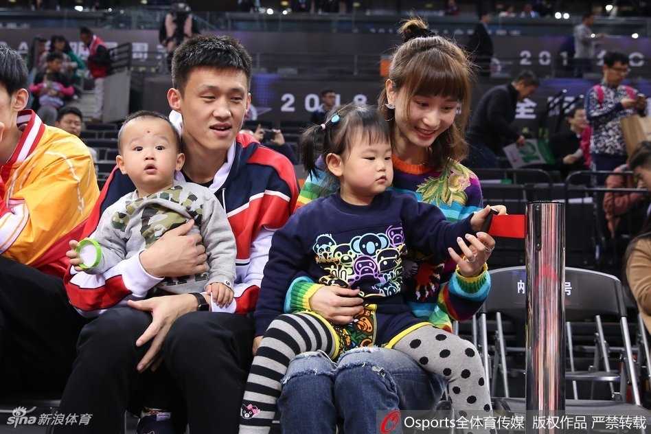 周鹏携家人观战星锐赛,铁血队长的温情一面 身着深色休闲装的周鹏将儿子轻抱在怀中,眼神温柔地看向镜头,身旁的女儿乖巧站立,妻子刘美则长发披肩面露微笑,一家四口在球场背景下显得格外温馨和谐