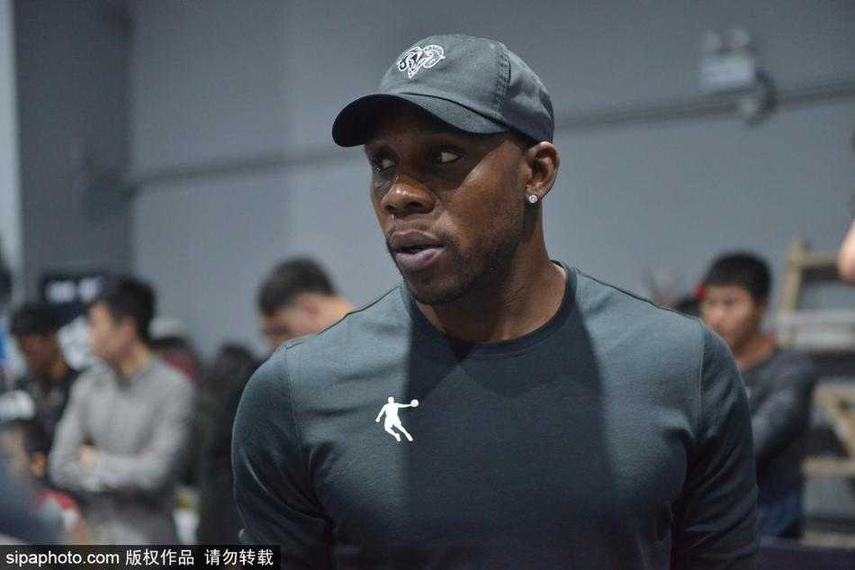 哈德森沈阳秀三分教女球迷运球 引爆篮球嘉年华 哈德森面带微笑,弯下腰耐心指导一位女球迷运球,眼神专注,场边围满了翘首以盼的观众。