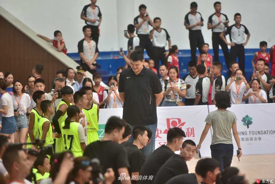 身高两米二六的姚明，在球场上弯下腰，几乎与身高仅及他腰部的小球员平视，眼神里满是鼓励与专注，画面既滑稽又温情