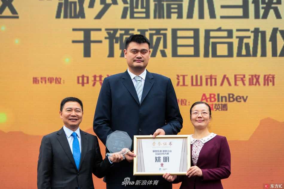 姚明现身校园开讲公益课,言传身教教会少年对饮酒说“不” 身穿深色上衣的姚明在校园教学楼前,被一群穿着红色校服的学生簇拥着,他面带微笑,亲切地拍着一位男生的肩膀,如同一位温和的邻家大哥哥。