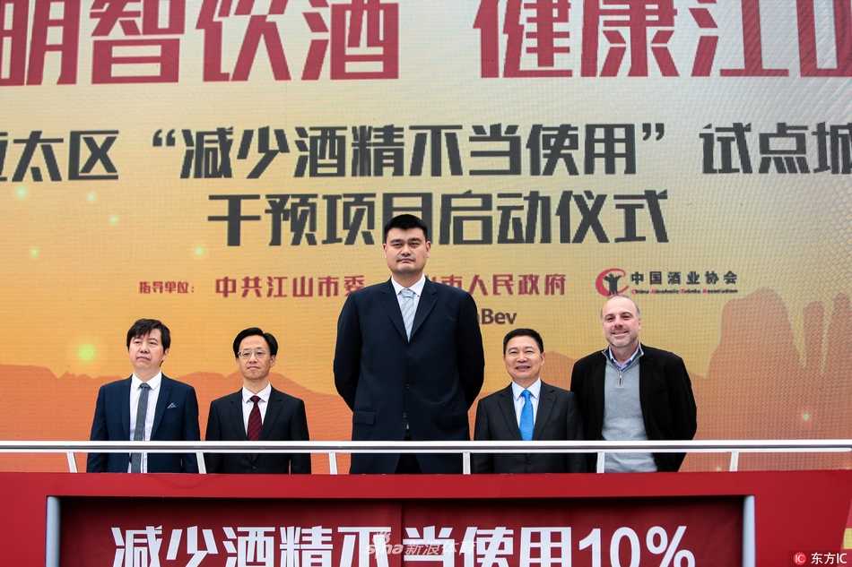 姚明现身校园开讲公益课,言传身教教会少年对饮酒说“不” 一位身穿黄色公益T恤的工作人员正在为同学们讲解展板上的酒精知识,背景是醒目的“明智饮酒 健康江山”活动标识,姚明站在一旁,认真地观察着同学们的反应。