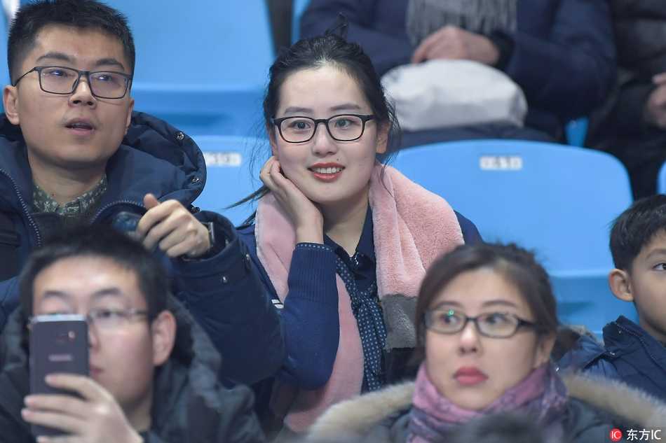 寒冬里的篮球火:吉林东北虎惜败上海,场边美女球迷惊艳长春 一位穿着白色毛领外套的年轻女性,面容清秀,坐在观众席前排,背景是模糊的赛场,她似乎正为吉林队错失的一次机会感到惋惜。