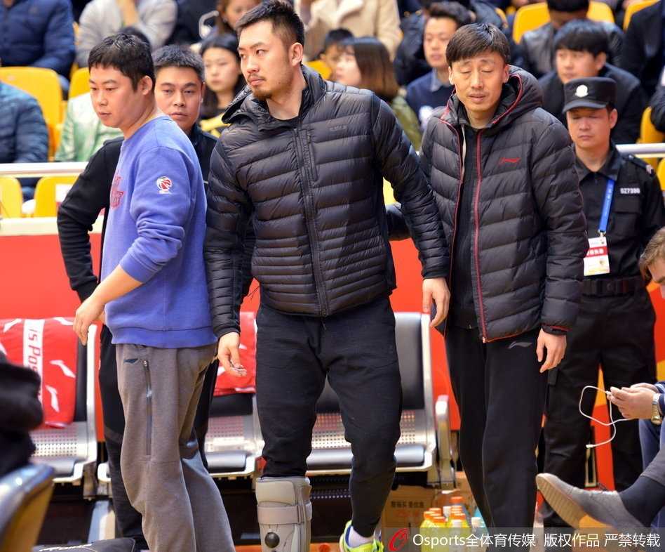 带伤观战神情凝重 睢冉缺阵山东加时险胜广厦 从高处俯瞰,睢冉独自一人坐在空荡的替补席区域,地板上散落着毛巾和球员物品,他左脚上的白色护具在一片深色座位中格外抢眼,整个场景充满孤寂感。