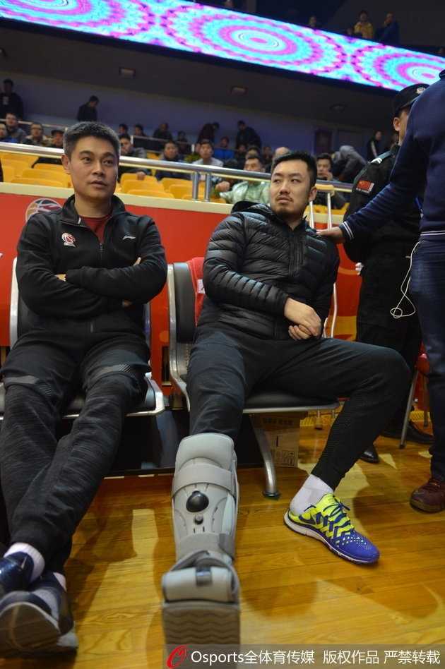 带伤观战神情凝重 睢冉缺阵山东加时险胜广厦 睢冉低着头坐在板凳席末端,左脚的保护靴被抬高搭在一个箱子上,他手中拿着一瓶水,表情显得有些落寞,与身后庆祝的球迷形成了鲜明对比。