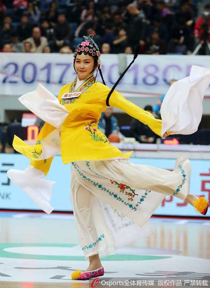 一位篮球宝贝的特写，她身穿粉色的戏曲改良服饰，手举助威花球，在赛场边笑容灿烂，华丽的头饰与现代化的体育场馆形成有趣的视觉对比。