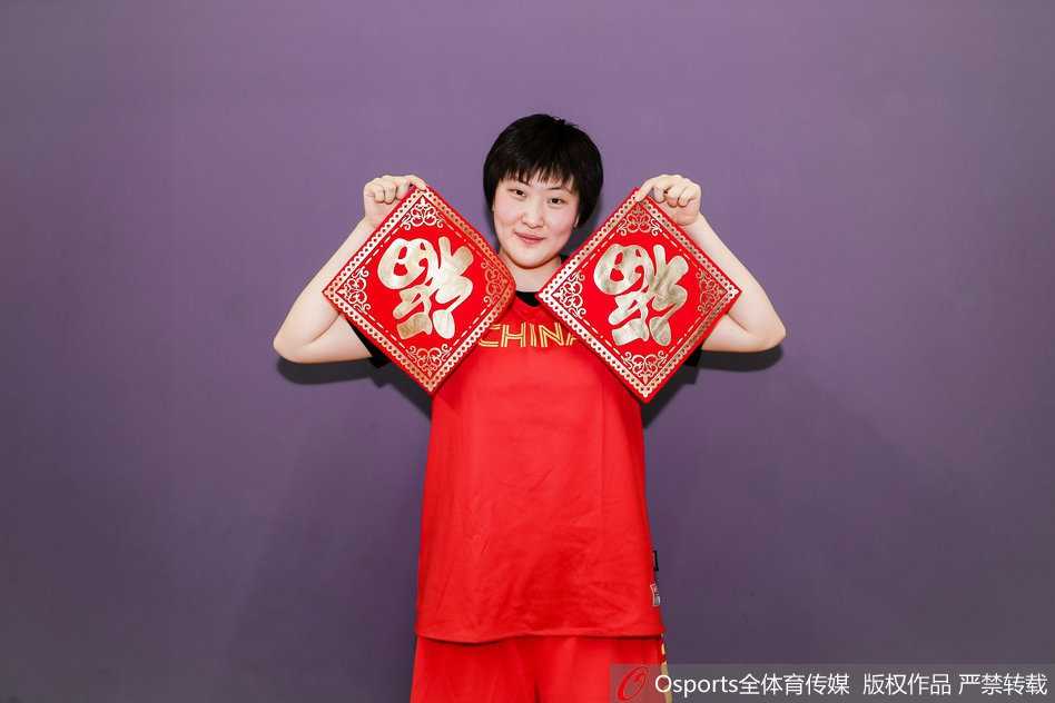 新春闪耀映红光,女篮精神铸辉煌 全体队员与教练组的大合影,大家簇拥在一起,有的竖起大拇指,有的挥舞着国旗,画面中充满了积极向上的能量,完美诠释了中国女篮团结拼搏的精神风貌。