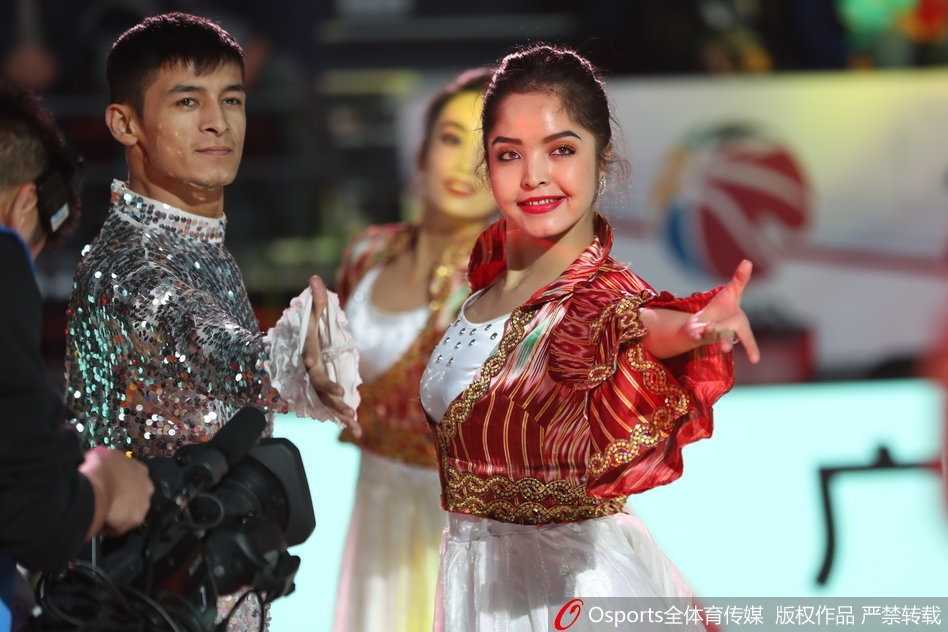 主场内，一位气质冷艳的西域美女回眸凝视，她的侧颜线条优美，长长的睫毛在灯光下投下阴影，身后的观众席虚化成一片热闹的背景。