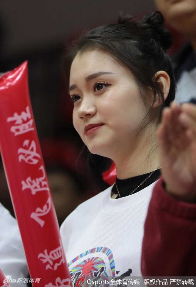 一位看起来年纪较小的学生球迷，穿着新疆队的队服，神情专注地为场上队员每一次精彩的配合鼓掌叫好。