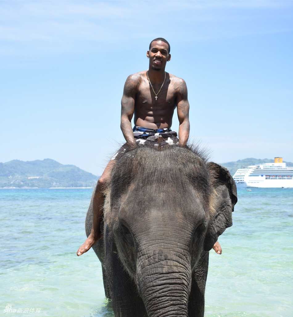 亚当斯在一处具有异域风情的建筑前驻足，他侧身对着镜头，背景是温暖的阳光和独特的建筑轮廓，整个画面呈现出一种悠然自得的度假氛围。