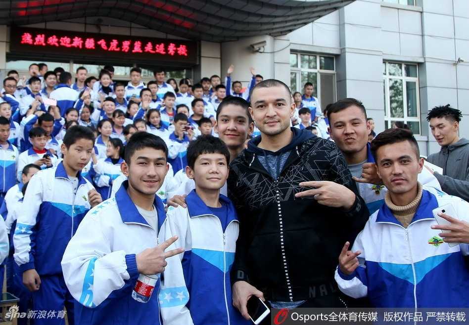 篮球架下，一位新疆男篮球员正弯下腰，手把手地纠正一位聋哑少年的投篮手型。少年仰着头，目不转睛地盯着偶像的手指，眼神里充满了专注与渴望学习的光芒。