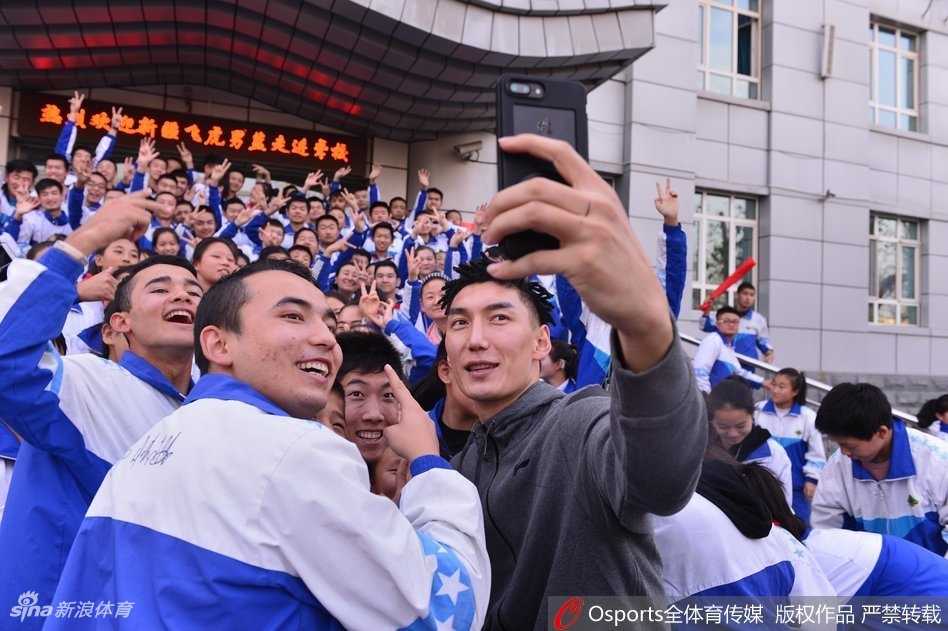 新疆广汇男篮的队员们集体亮相聋人学校操场，他们微笑着与穿着校服的孩子们站在一起，阳光洒在每个人身上，大手拉小手，无声的问候在此刻胜过千言万语。