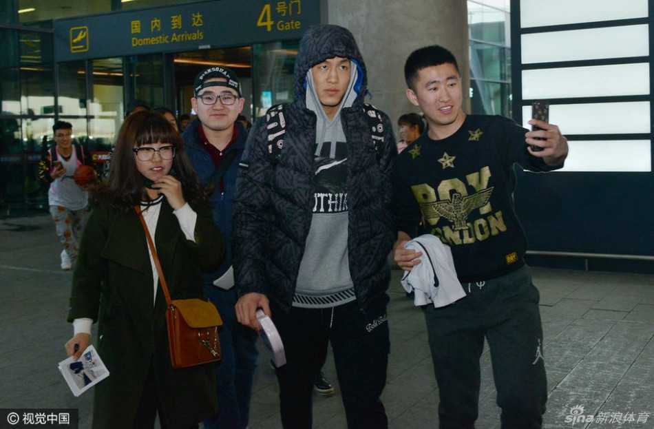 身穿黑色长款羽绒服的郭艾伦神态亲和，微微弯腰俯身，正在为一位身着蓝色辽篮球衣的小球迷认真地签名，周围是无数高举手机记录这一刻的热情人群。