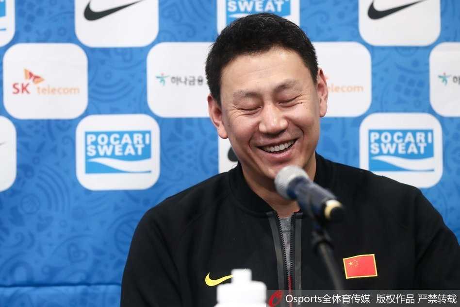 李楠面对镜头露出腼腆的微笑，嘴角上扬，展现出铁血主帅难得一见的羞涩一面