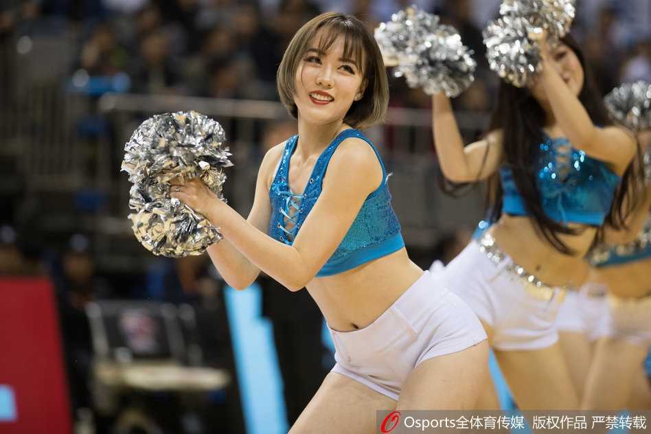 全景视角下，一群篮球宝贝侧身排开，高举双手舞动，现场地板反射着灯光，营造出热烈的赛场氛围