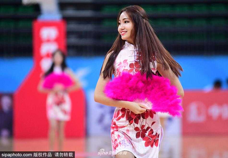 在球场炫目的灯光下，旗袍宝贝们整齐划一地扬起手中金色的花球，她们身上的旗袍颜色鲜艳，红色与金色交织出喜庆热烈的赛场氛围。