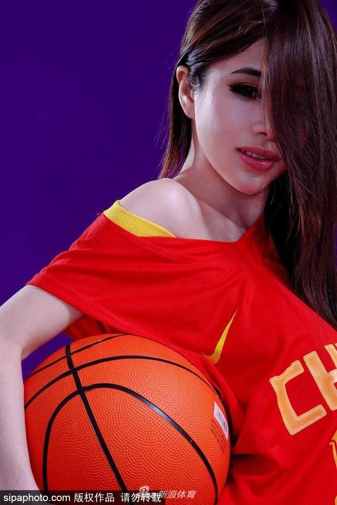 袁颖芬身着时尚运动装，双手持球举过头顶，脸上洋溢着灿烂笑容，健康的小麦色肌肤在阳光下闪闪发光，完美诠释了力挺男篮的动感与热情。