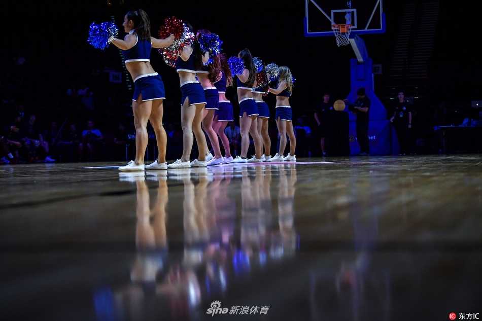 两位啦啦宝贝近距离特写，她们额头微微出汗，却依然保持着标准的露齿笑容。身后的篮球架和看台虚化为背景，更凸显了她们作为赛场焦点的自信与美丽。