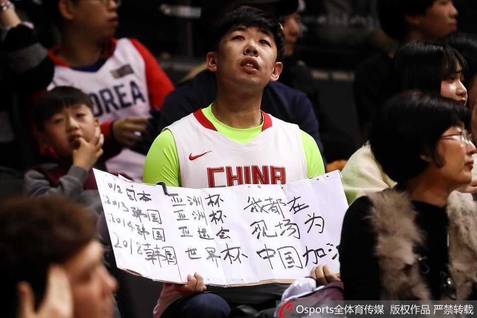 热血与颜值齐飞:篮球架下那道最美的风景线 这位戴着可爱发卡的女生正对着镜头比出胜利的手势,她的笑容如同冬日里的暖阳,灿烂而治愈,手中的加油牌在灯光下熠熠生辉,仿佛整个赛场都被她的热情所感染。