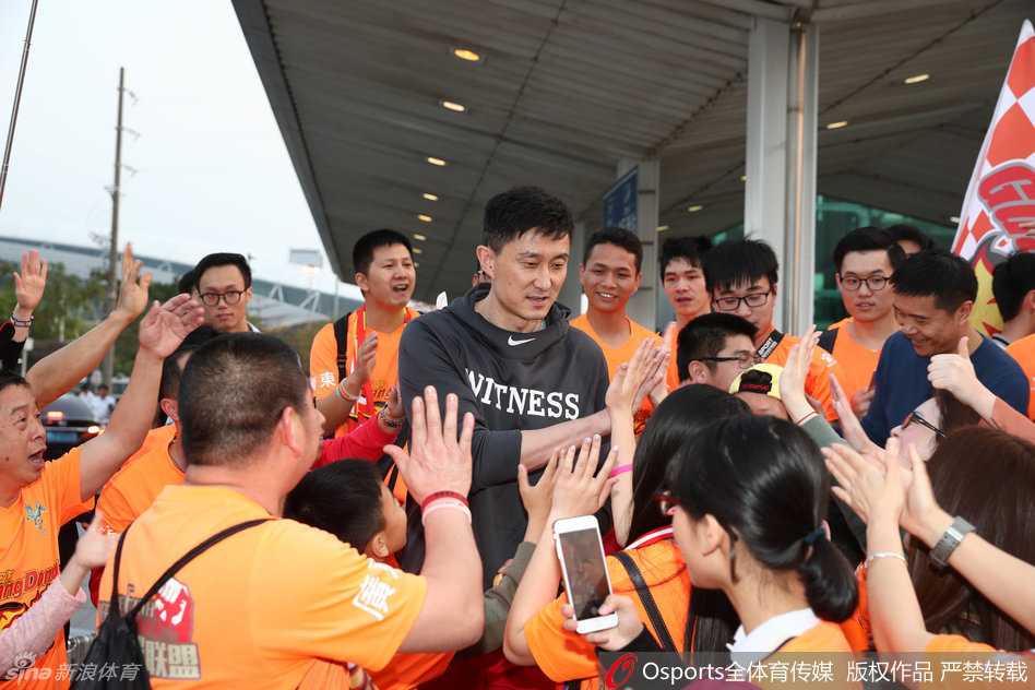 人潮人海中，主教练杜锋被热情的球迷紧紧簇拥在中间，球迷们高举手机记录着偶像归来的瞬间，场面热烈。