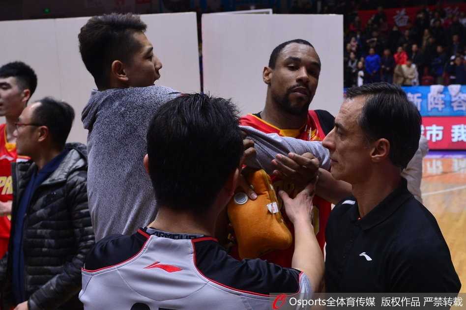 疆深赛后火爆冲突,外援萨林杰怒踹广告牌 从侧面看去,萨林杰被围堵在人群中,他的眼神死死盯着新疆队球员离开的方向,双臂被队友紧紧锁住,肌肉紧绷,仿佛下一秒就要挣脱束缚。