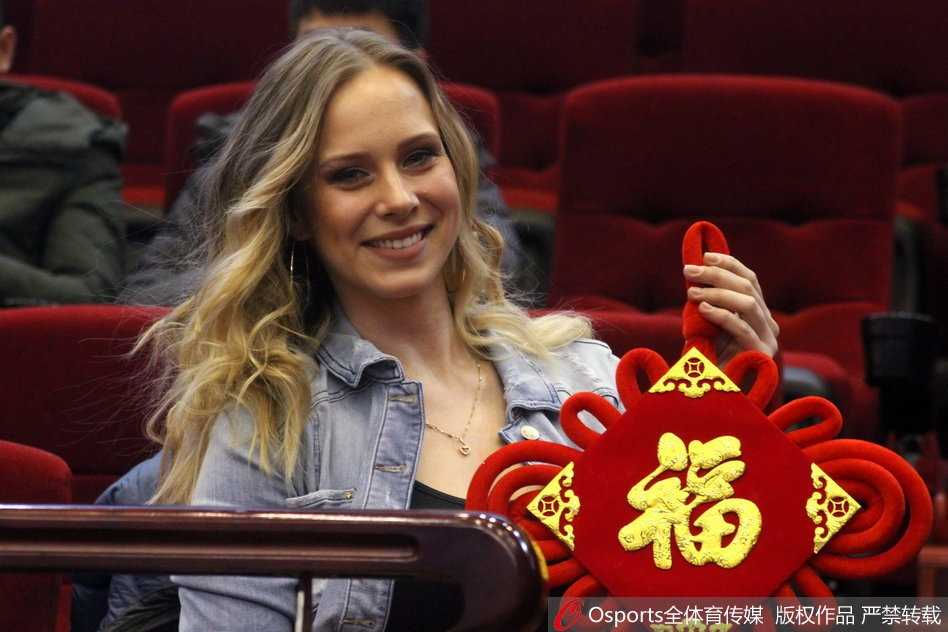 莫泰尤纳斯的爱妻身披一袭暖冬装扮，双手轻展写有福字的红纸，那灿若星辰的湛蓝眼眸中盛满了对爱人比赛的期许，温婉笑意间流露出东欧女性独有的典雅韵味。