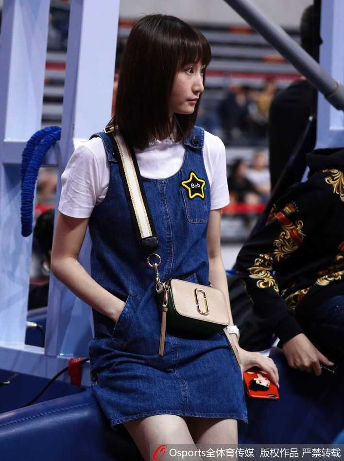 镜头拉近，刘美的侧颜精致立体，微微扬起的下巴带着一丝骄傲。她静静地坐在那里，仿佛能给予场上拼搏的丈夫无形的力量，牛仔裙的剪裁完美勾勒出她的优雅身姿。