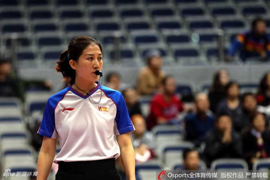 女裁判侧身站立，神情严肃地记录着场上的犯规情况，场边的广告牌映衬出她专注的身影