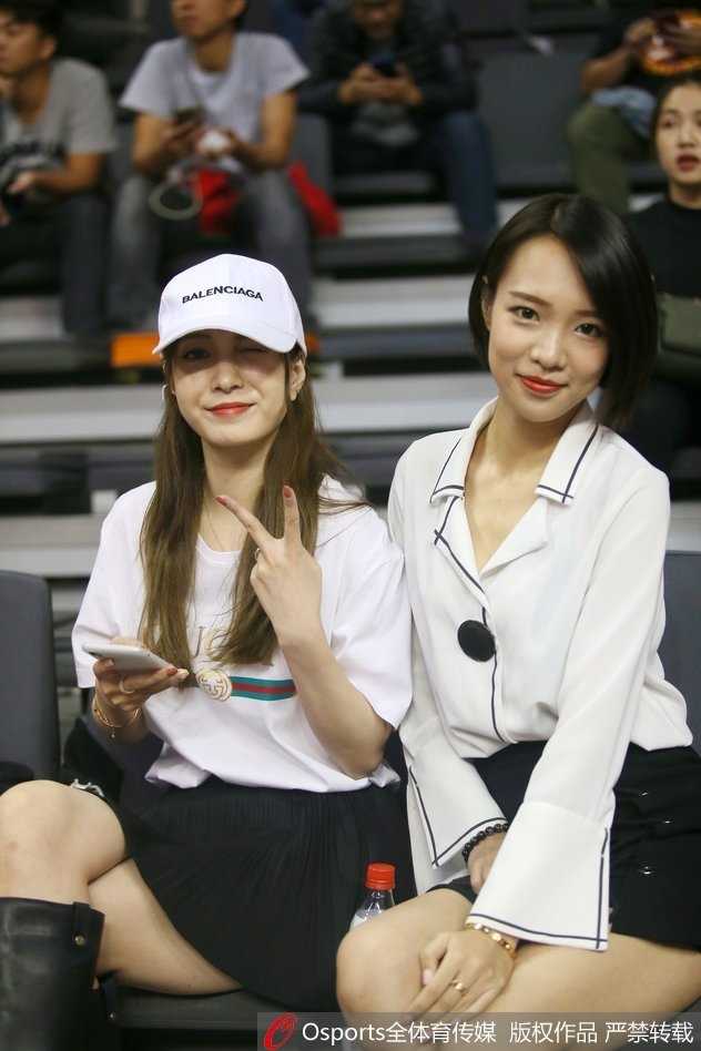 一位气质温婉的女球迷坐在看台前排，背景是激烈的比赛画面，她仿佛沉浸在自己的篮球世界中，温润如玉。
