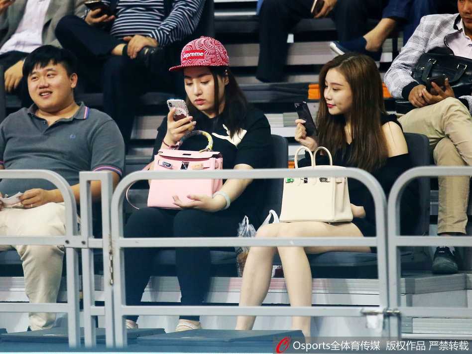 一位面容清秀的女球迷坐在场边，目光越过喧嚣，专注地望向赛场方向，仿佛与周遭的紧张气氛隔绝。
