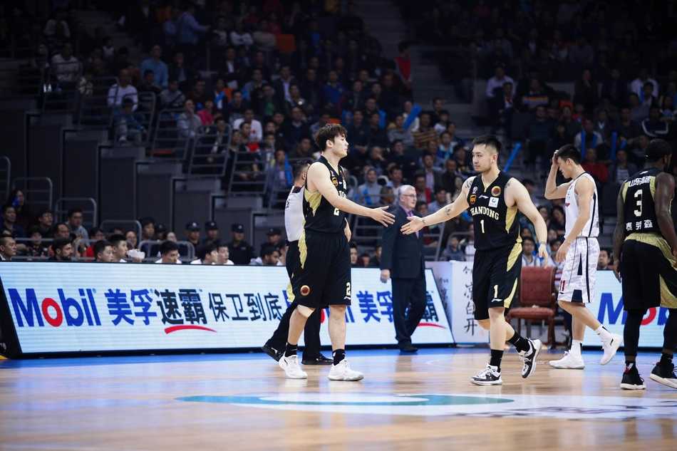 山东队核心丁彦雨航持球强行突破国家队老大哥周鹏的严防死守，两人肌肉碰撞，眼神中充满了对胜利的渴望，仿佛整个球场都成为他们的角斗场。