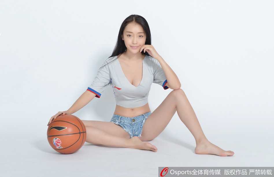 一位篮球宝贝低头看着手中的篮球，仿佛在思考接下来的“判罚”，她的侧脸线条柔和，裁判服胸前的口哨格外醒目，身后是正在热身的球员，动静之间构成一幅和谐的画面。