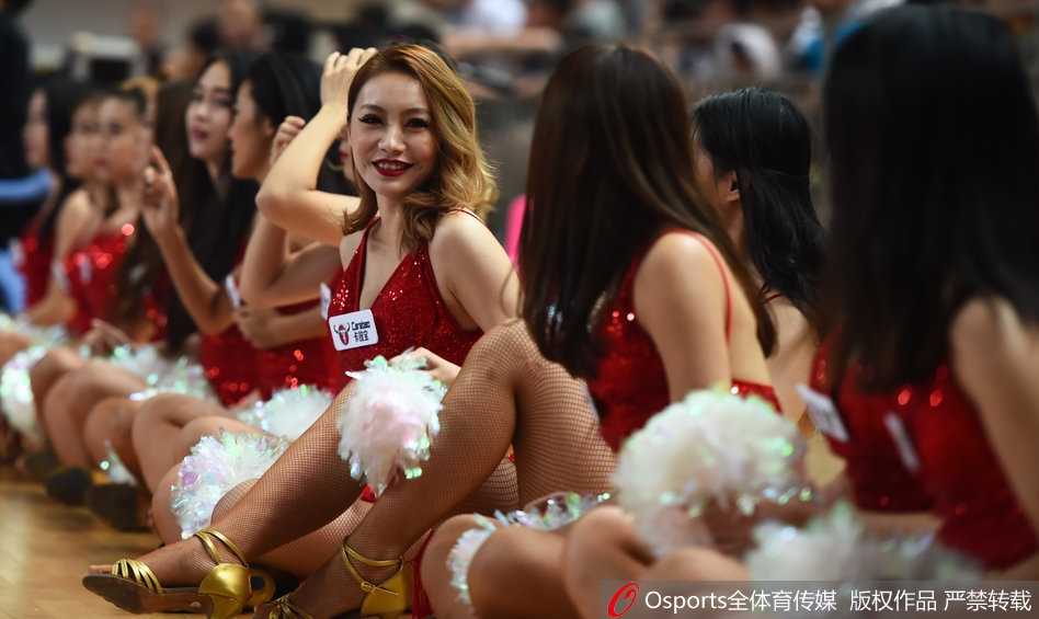 红裙啦啦队领舞者激情绽放，长发飘飘，眼神充满感染力，身后的记分牌映衬着赛场的紧张