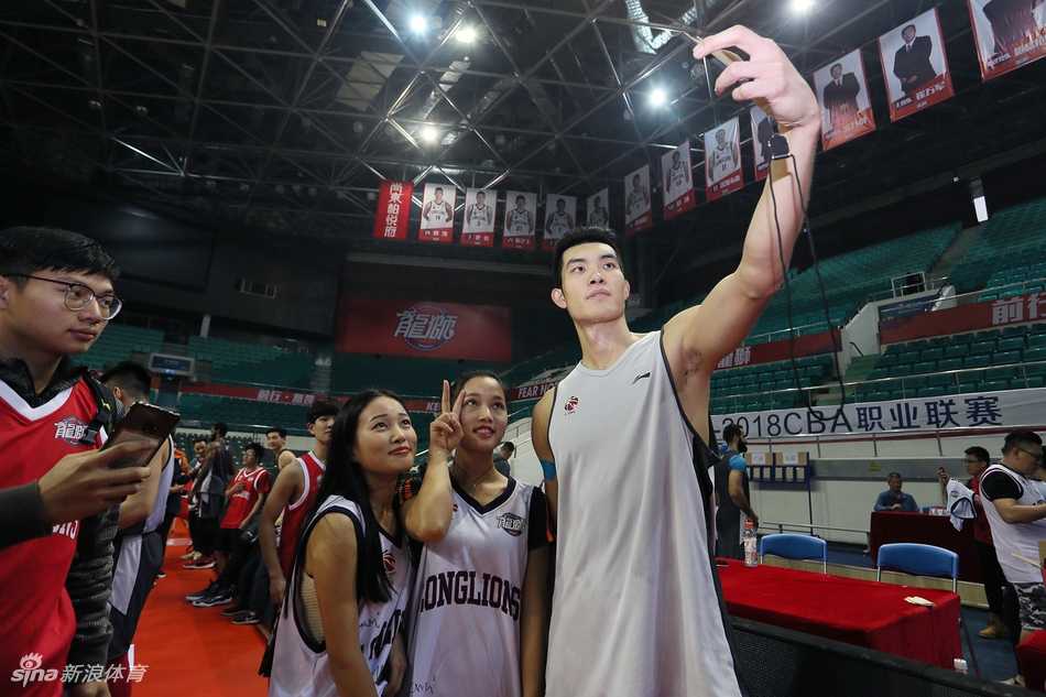 广州男篮的多名队员并排坐在场边长椅上，手中拿着签字笔，正在为身前排队的数十名球迷手中的纪念品签名，场面秩序井然。