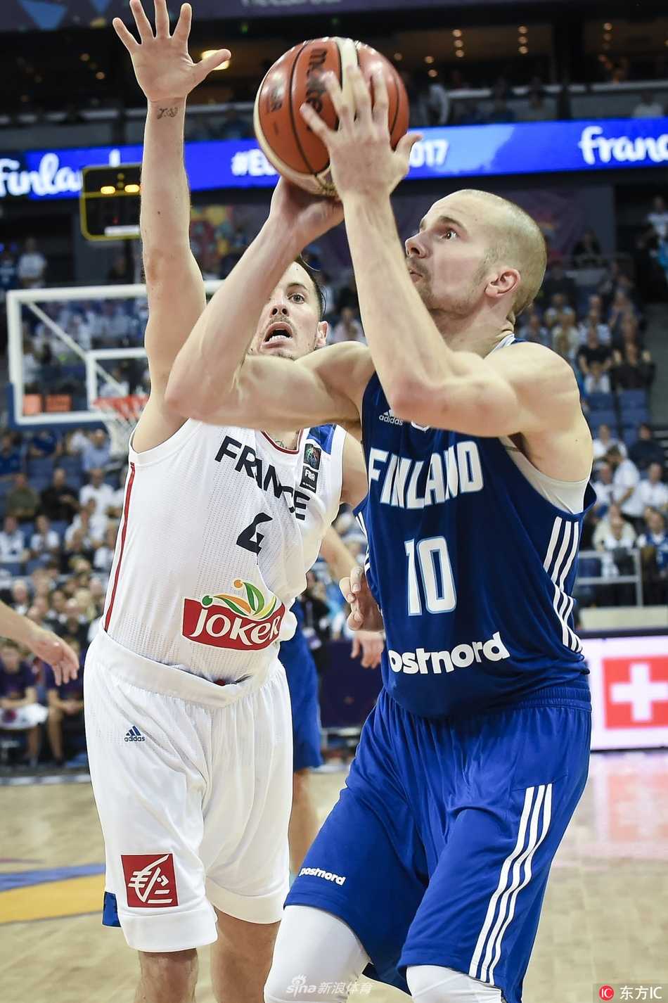 芬兰队7号新星马尔卡宁面对法国防守球员，高高跃起，眼神坚定地投出三分球的瞬间，全场球迷屏息凝视。
