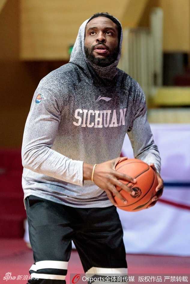 哈达迪在进行拉伸训练，表情略显疲惫但眼神坚毅，手中的热饮在寒冷的球馆里升起袅袅白气。