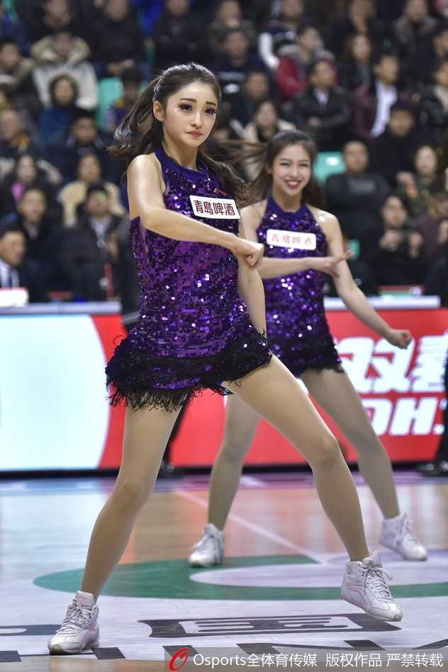 辽宁啦啦队宝贝身披白色绒衣在场边热身，回眸瞬间眼神灵动，带着羞涩而甜美的笑容，仿佛冰雪中绽放的玫瑰，为即将到来的热舞积蓄能量。