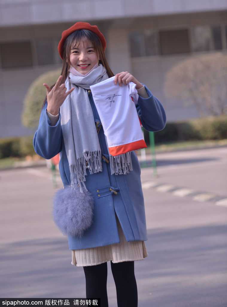 一位短发女球迷双手捧着篮球和照片，神情专注而紧张地望着球员通道，仿佛下一秒她的偶像就会出现，完成她期待已久的签名。