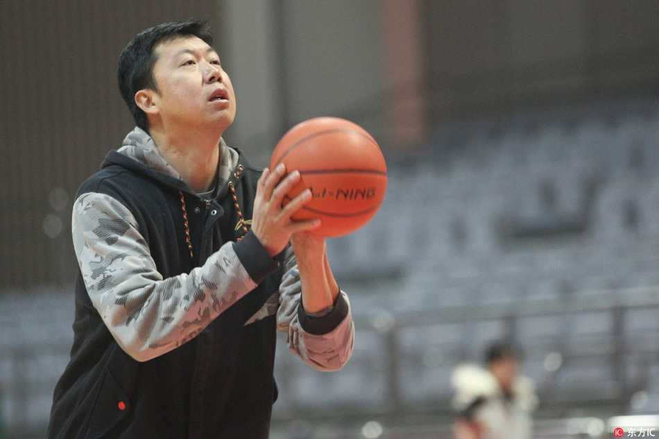 王治郅在训练馆中央背身持球，眼神专注地盯着篮筐，准备向年轻球员演示内线进攻步伐。