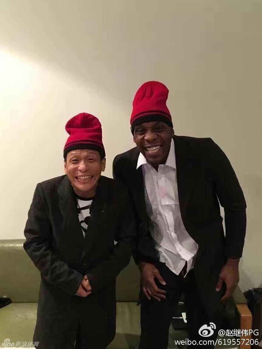 彩排现场灯光昏暗，哈德森身穿灰色西装，表情严肃地用手指着前方，仿佛在小品中遇到了什么让他震惊又好笑的事儿。