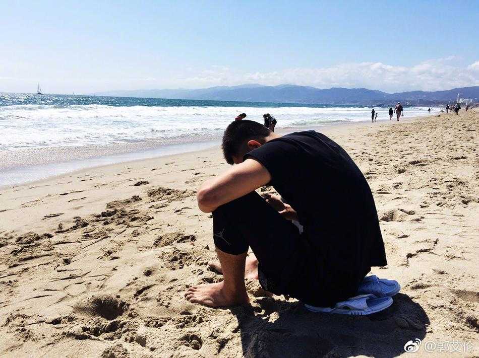 阳光洒在郭艾伦的笑脸上，他穿着休闲T恤，在海滩的微风中惬意地啃着金黄喷香的烤苞米，眼神里都是放松。