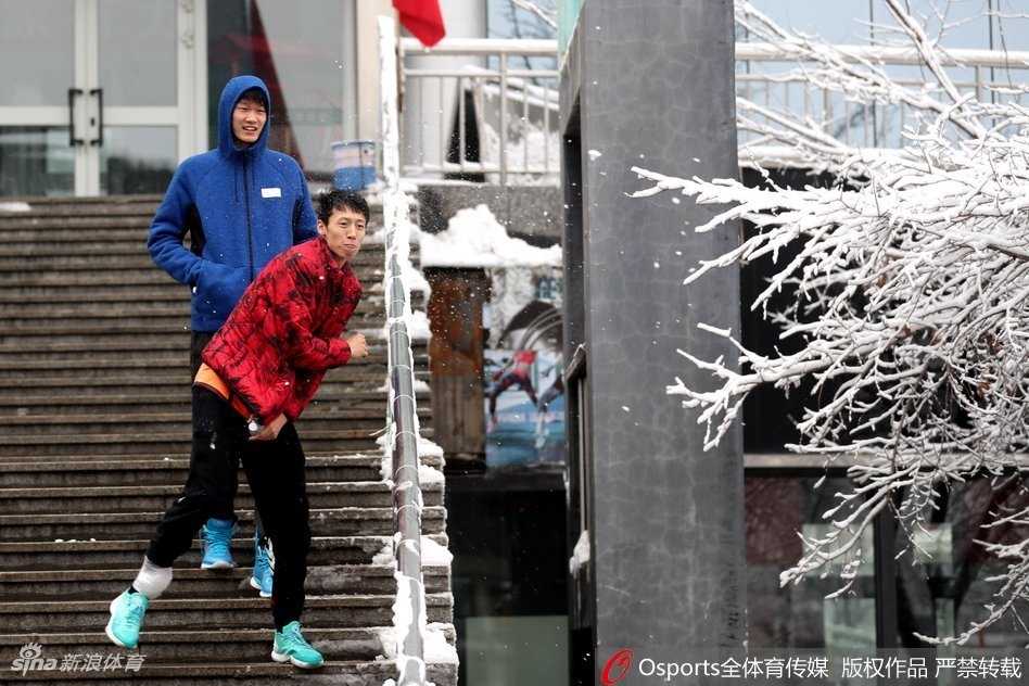 广厦球员在乌鲁木齐雪地中漫步，一行人在雪地上留下深浅不一的脚印，背景是冬日里静谧的城市景色。